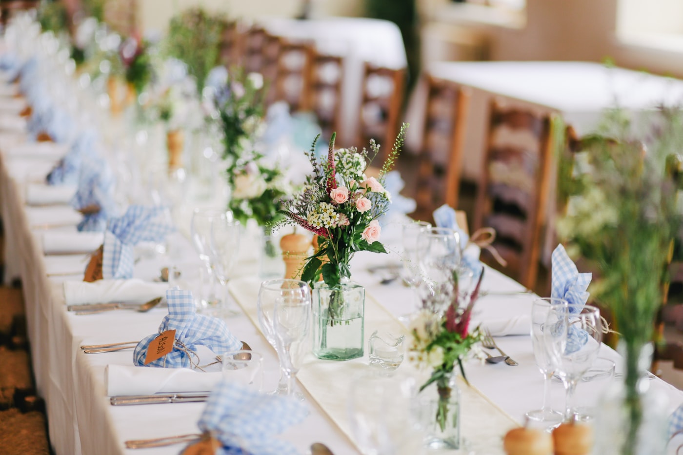 A long table set with white linens, glassware, and wildflowers for a gathering