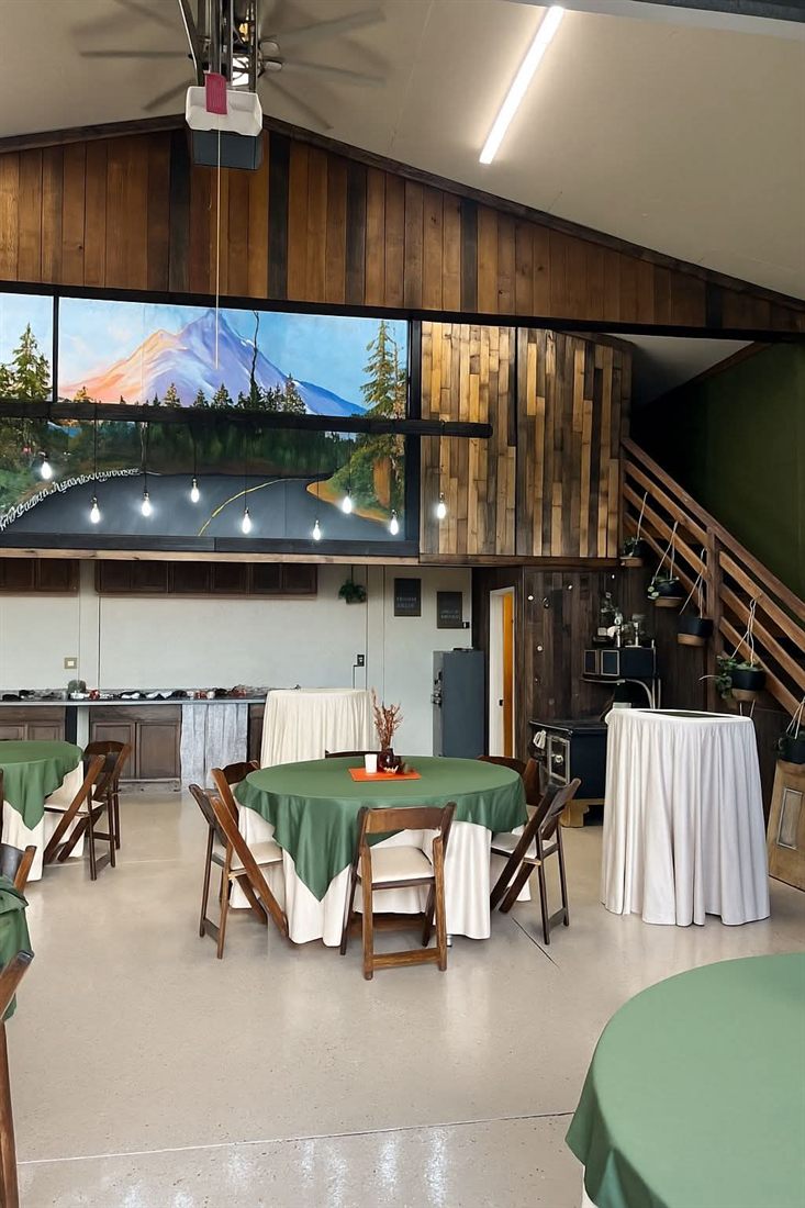 Christy's event space set with round and bistro tables beneath a painted mountain mural